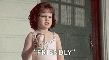 a little girl in a white dress is holding a can of soda and saying `` friendly '' .