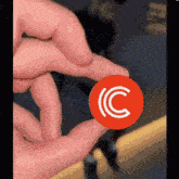 a person is holding a red circle with a white c on it