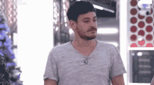 a man with a beard is wearing a grey t-shirt and a necklace while standing in a room .