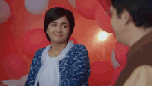 a woman in a blue jacket looks at a man in front of balloons