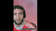 a man wearing headphones and a red shirt is covering his eyes with his hand .