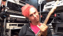a man with pink hair is playing a guitar in front of a rack of electronics including an akai
