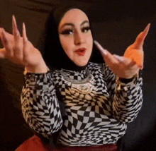 a woman wearing a hijab and a checkered shirt is making a gesture with her hands