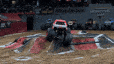 a monster jam sign is behind some monster trucks on a dirt track