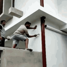 a man is painting a wall with a brush while another man watches .