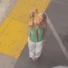 a woman in a green top and white pants is holding a rose