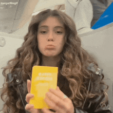a woman in a leather jacket is holding a yellow book that says " margaritosgif " on the bottom