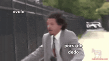 a man in a suit and tie is running down a street with the words porra do dedo written on the bottom