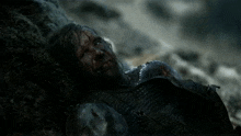 a man with blood on his face is laying on a rock