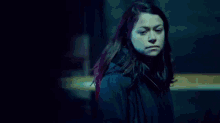 a woman in a black coat is standing in a dark room looking at the camera