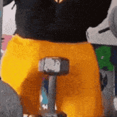 a man in yellow shorts is holding a dumbbell in his hand .