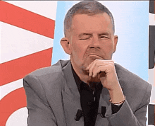 a man in a suit is sitting in front of a red and white sign with his hand on his chin .
