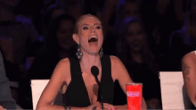 a woman is sitting in front of a microphone with her mouth open and a cup of soda in front of her .