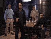 a group of men are clapping in a dark room with a table and chairs