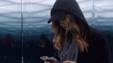 a woman wearing a hooded jacket and a hat looks at her phone