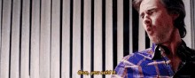 a man in a plaid shirt is standing in front of a striped wall and talking to someone .