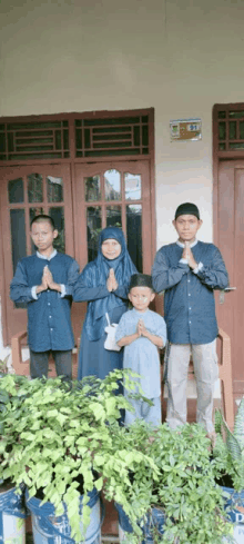 a group of people standing in front of a house with their hands folded in prayer