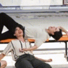 a man is laying on his back on a bench while another man sits next to him
