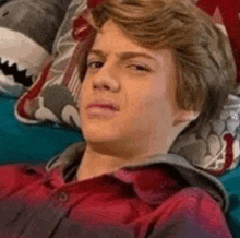a young man is laying on a couch with a shark pillow .