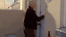 an older man is knocking on a door with a bottle of beer in front of him .