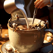 a person is pouring milk into a cup of coffee surrounded by miniature people .