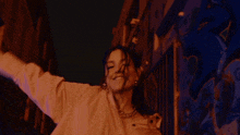 a woman in an orange shirt is dancing in front of a wall with graffiti on it