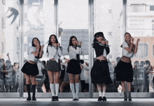 four girls in school uniforms are dancing in front of a large window