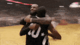 a couple of basketball players hugging each other on a court .