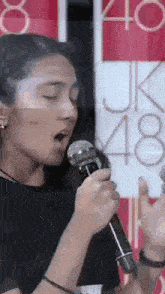 a woman is singing into a microphone in front of a sign that says 48 .