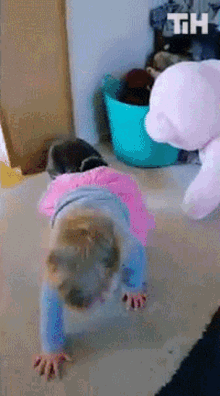 a little girl is crawling on her knees next to a teddy bear and a blue bucket