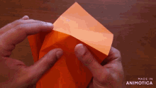 a person is folding an orange piece of paper and the words made in animotica are visible