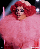 a drag queen is wearing a pink costume with a large pink ruffled collar