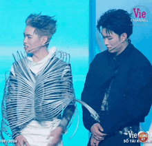 a couple of men are standing next to each other on a stage . one of the men is wearing a strange costume .
