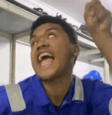 a man in a blue shirt is making a funny face with his mouth open and his fist in the air .