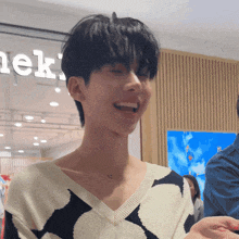 a man wearing a black and white sweater smiles in front of a sign that says ' ek ' on it