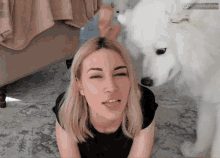 a woman laying on the floor with a white dog looking at her face .