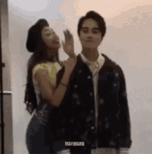 a man and a woman are standing next to each other . the woman is whispering into the man 's ear .