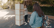 a man is carrying a large piece of furniture next to a woman who is carrying a backpack .