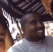 kanye west is smiling while sitting next to a woman in a restaurant .