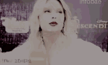 a woman with blonde hair and red lipstick is standing in front of a sign that says ' disney ' on it .