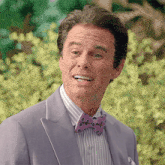 a man wearing a purple suit and a bow tie smiles