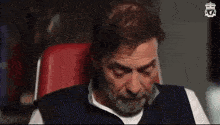 a man with a beard is sitting in a chair with his eyes closed and his hands on his chest .
