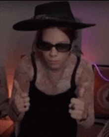 a woman wearing a hat and sunglasses is giving a thumbs up sign .