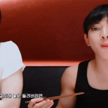 a man in a black tank top is holding chopsticks