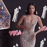 a woman in a silver dress is standing on a red carpet at a music video awards event .