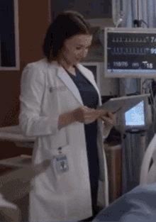 a woman in a lab coat looks at a tablet in a hospital room