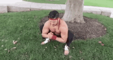 a shirtless man is squatting on the grass in a park .