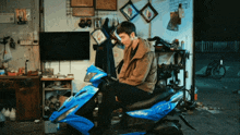 a man sits on a blue scooter in front of a tv