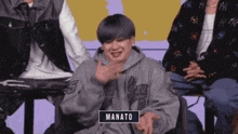 a man wearing a hoodie with the name manato on it is sitting in a group of people .