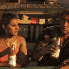 a man and a woman are sitting at a table holding bottles of alcohol